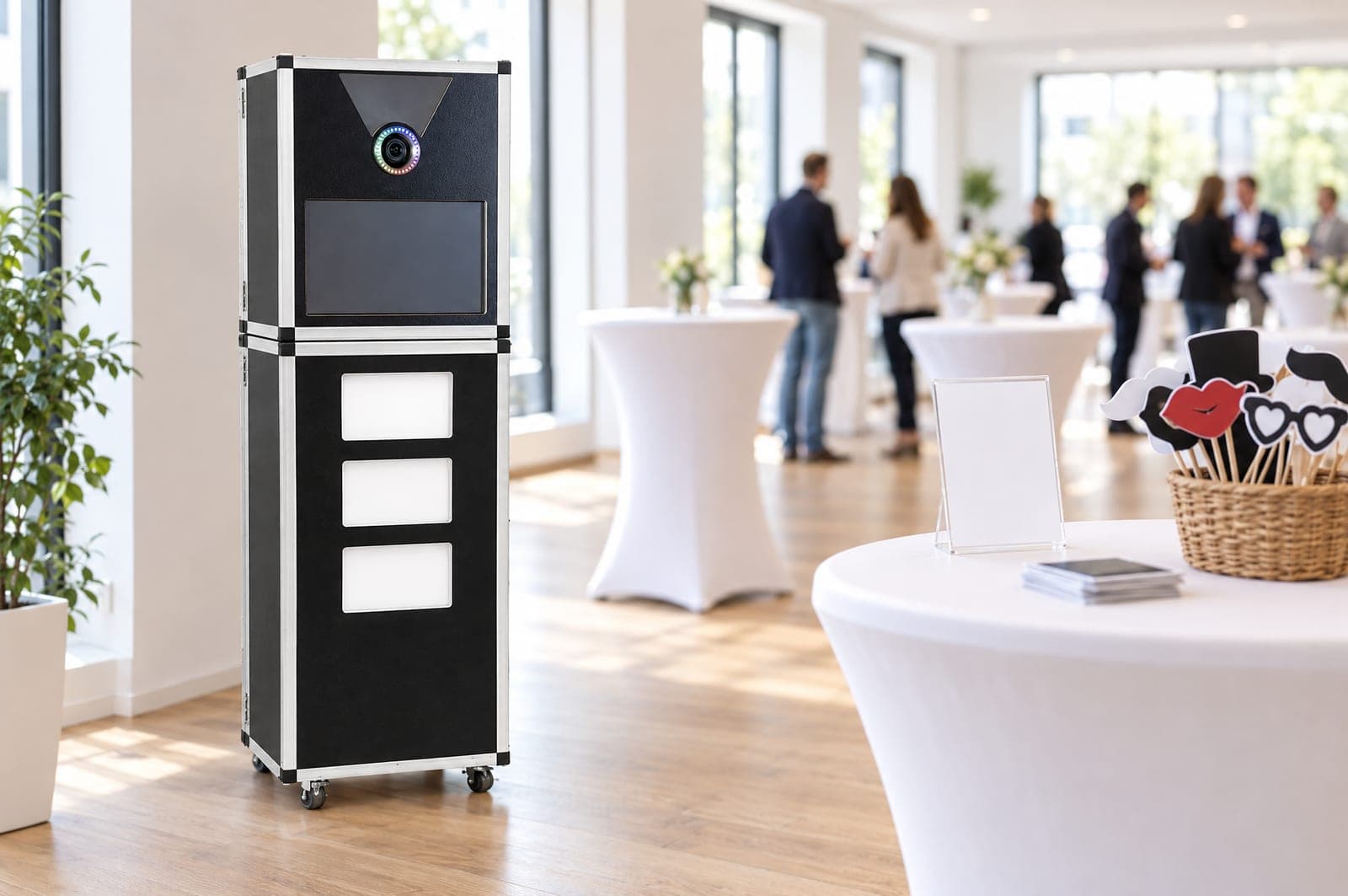 Stehtisch neben der Premium Fotobox mit leerem Hinweisschild-Aufsteller, verdeckt liegenden Ausdrucken und Requisitenkorb in einem hellen Veranstaltungsraum