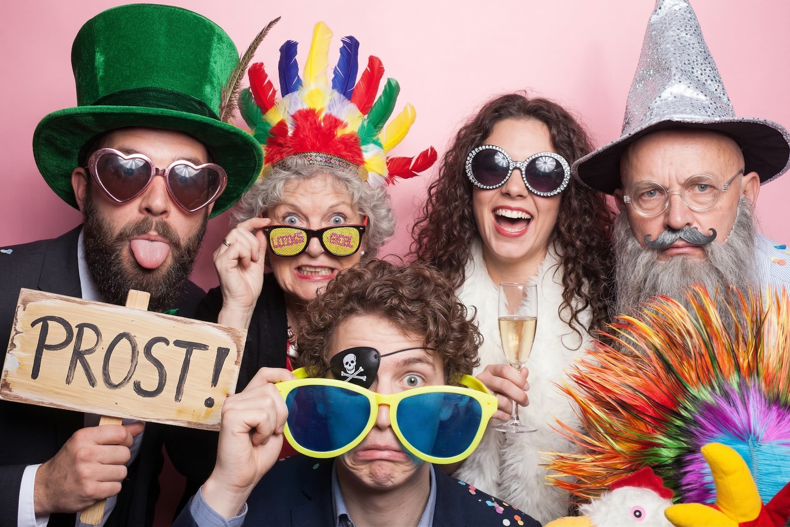 Fünf Gäste feiern in der Fotobox mit Verkleidungen und Prost-Schild